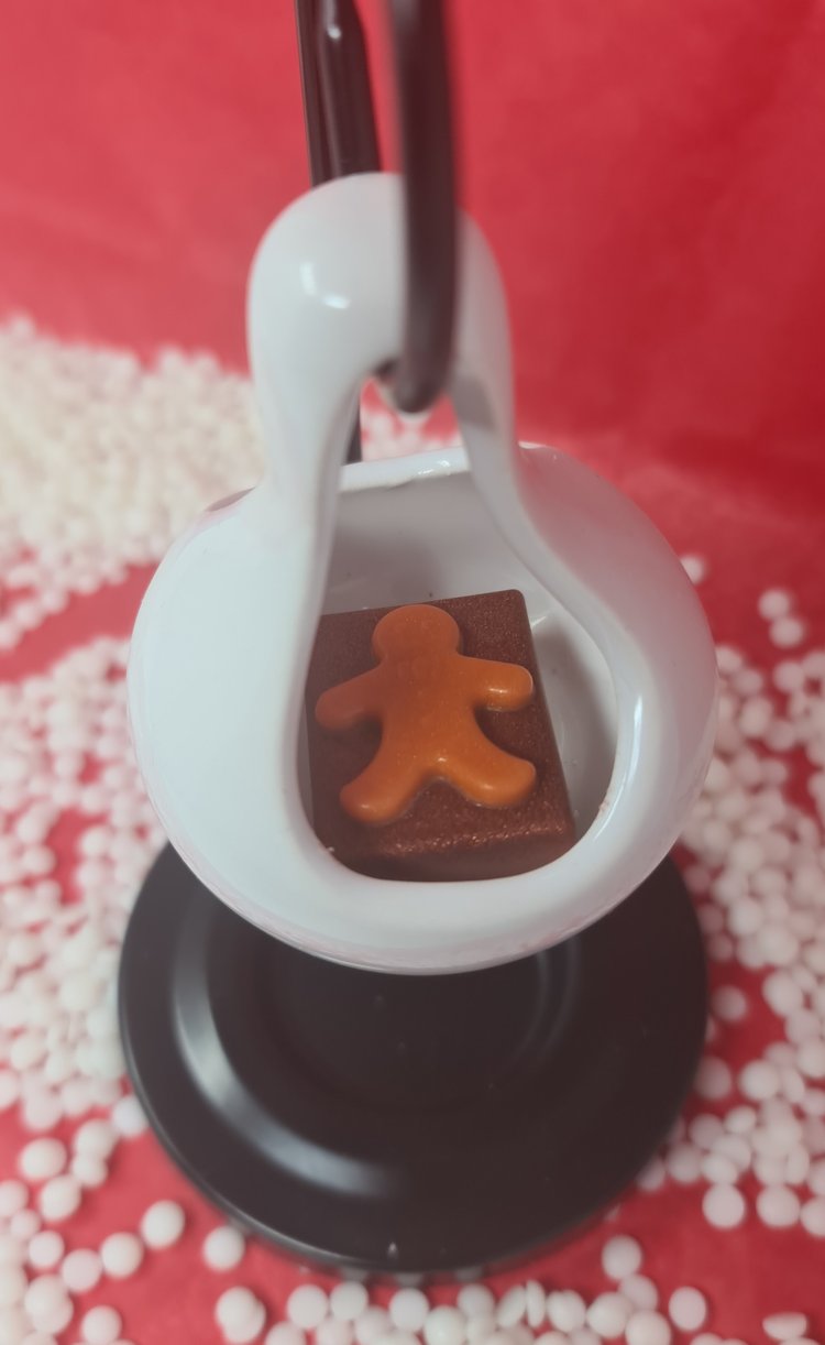 Christmas wax melt shaped like a gingerbread man in a white holder with festive background.