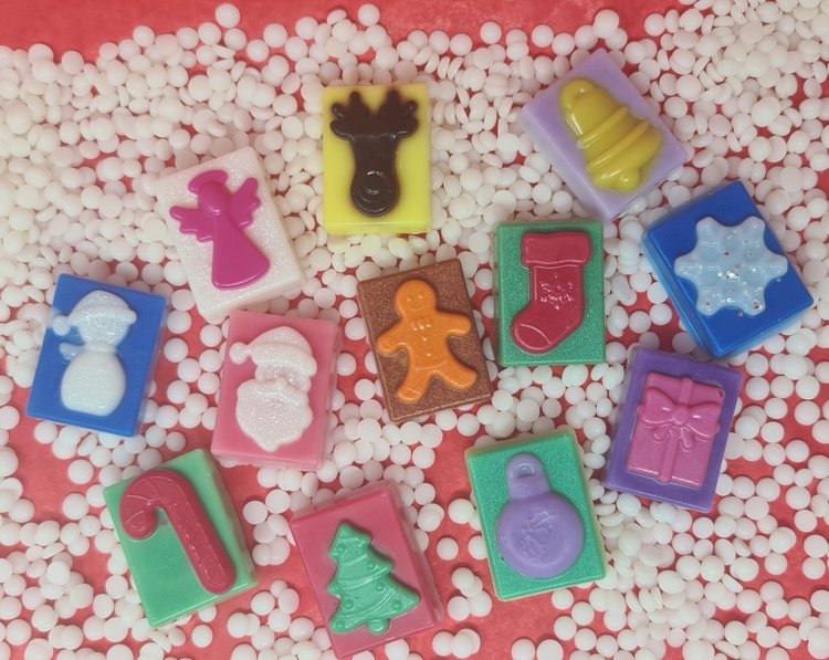 Colorful Christmas-themed wax melts in various shapes surrounded by white beads.
