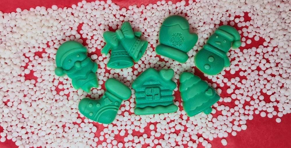 Christmas-themed scented wax melts in shapes like Santa, bell, snowman, stocking, glove, cabin, and Christmas tree, displayed on a red and white background.