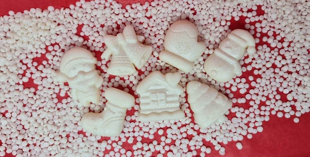 Christmas themed scented wax melts with Santa, bell, snowman, stocking, glove, cabin, and tree designs on a festive background.