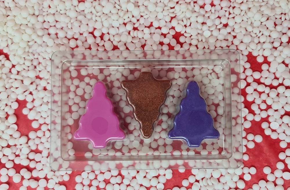 Colorful Christmas tree scented wax melts in a clear tray on a festive background.