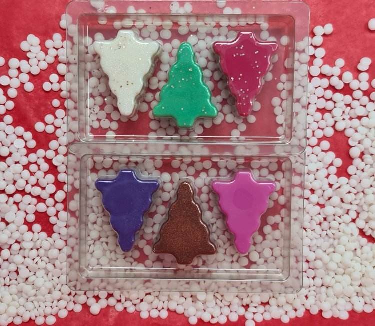 Colorful Christmas tree shaped scented wax melts in transparent packaging on a festive background.