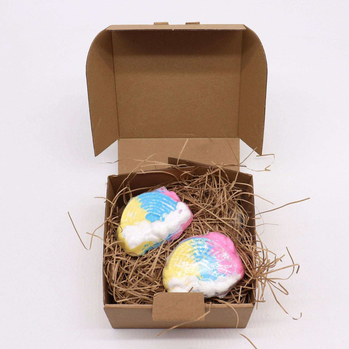 Cloud Bath bomb in whimsical cloud shape with yellow, blue, pink, and white colors nestled in brown shredded paper inside an open cardboard box