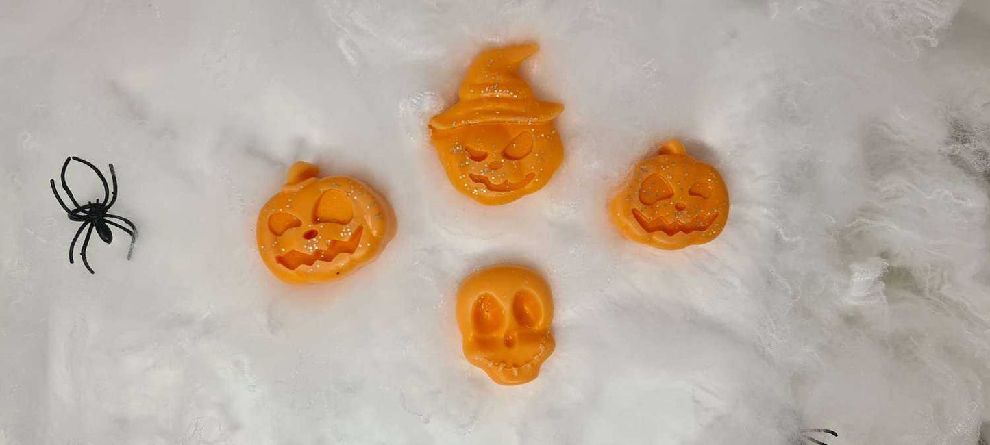 Large pumpkin and skull pumpkin spiced wax melts on a cloudy background with decorative spider.