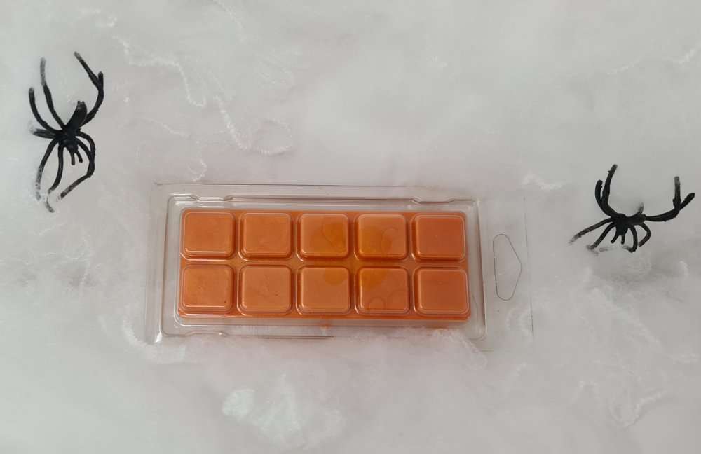 Orange pumpkin-themed wax melt clamshell with 10 segments, surrounded by Halloween decorations.