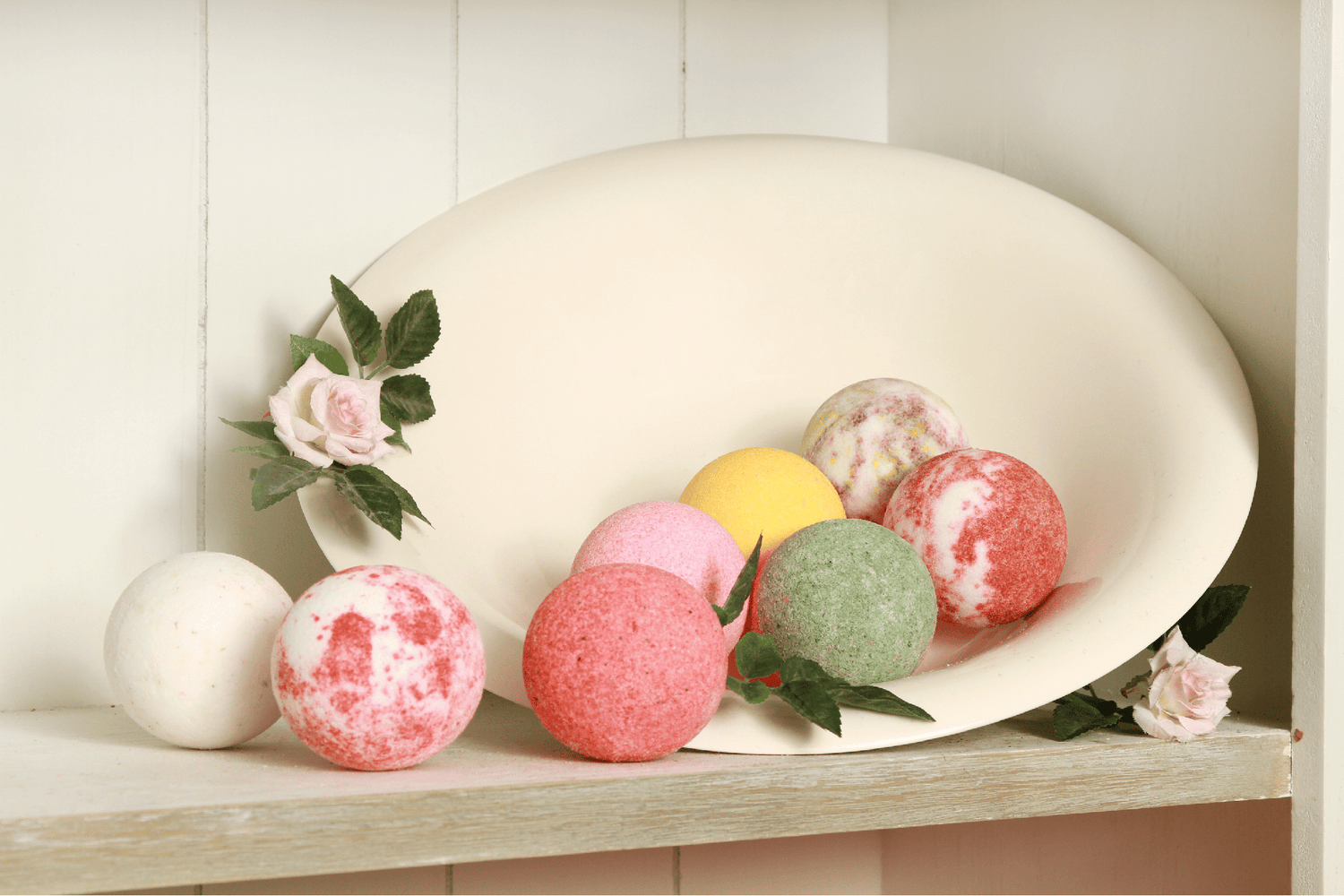Jumbo multicoloured bath bombs nestling in a tray with pink roses