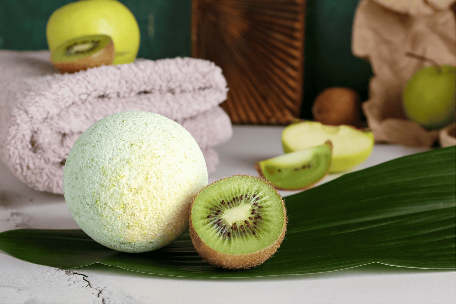 Green bath bomb with Kiwi fruit and plant with a towel in the background