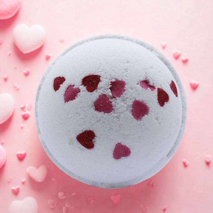 Love Hearts Bath Bomb with red heart decorations on white fizzing sphere against pink background