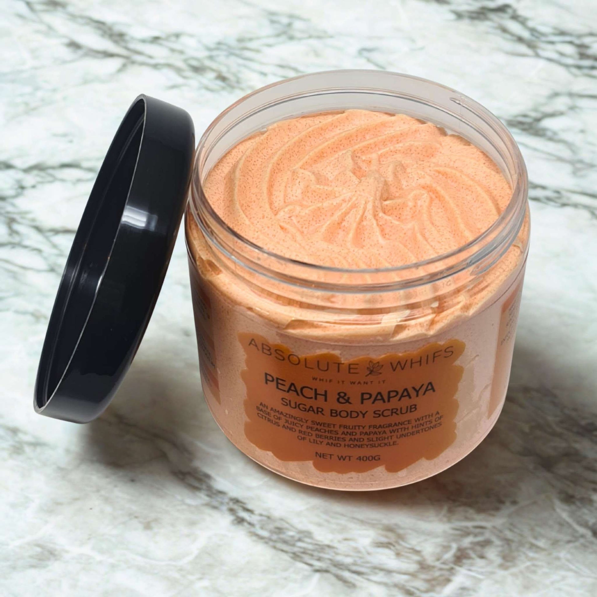 Peach and papaya sugar body scrub in clear jar with black lid on marble surface
