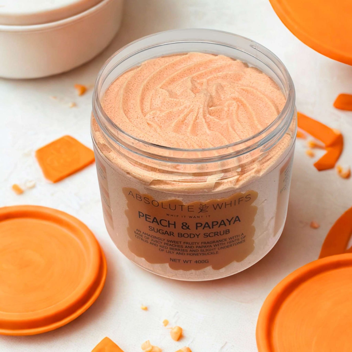 Peach and papaya sugar body scrub in clear jar with orange lid and creamy texture