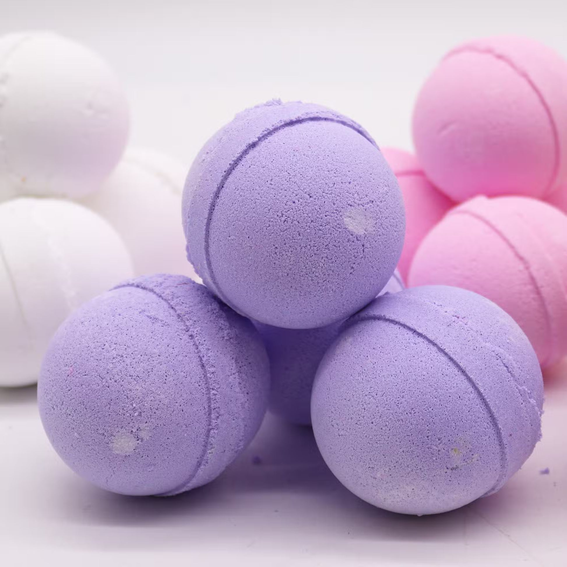 Purple blackberry bath bombs stacked with pink and white bath bombs in the background, 180g luxurious fizzer for relaxing baths