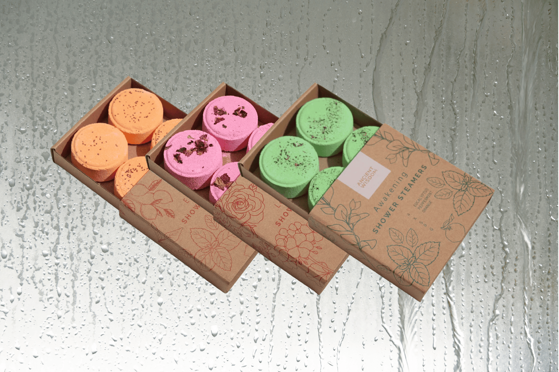 Valentines Pamper Hamper shower steamer sets with orange, pink, and green bath steamers in sliding kraft boxes on wet glass background