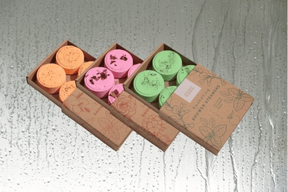 Valentines Pamper Hamper shower steamer sets with orange, pink, and green bath steamers in sliding kraft boxes on wet glass background
