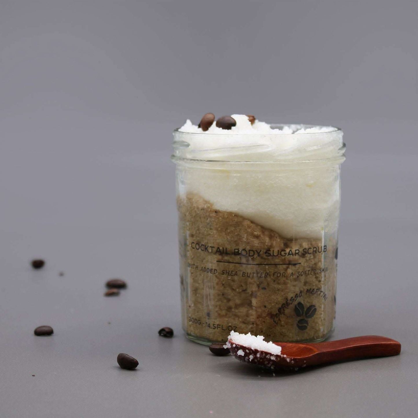 Fragranced sugar body scrub in a jar with coffee beans and wooden spoon on gray background