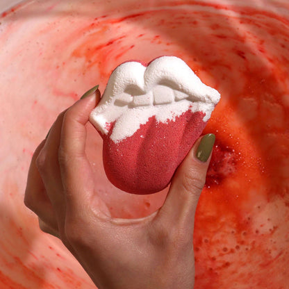 Hand holding lips-shaped bathbomb with raspberry and pomegranate scent fizzing in water