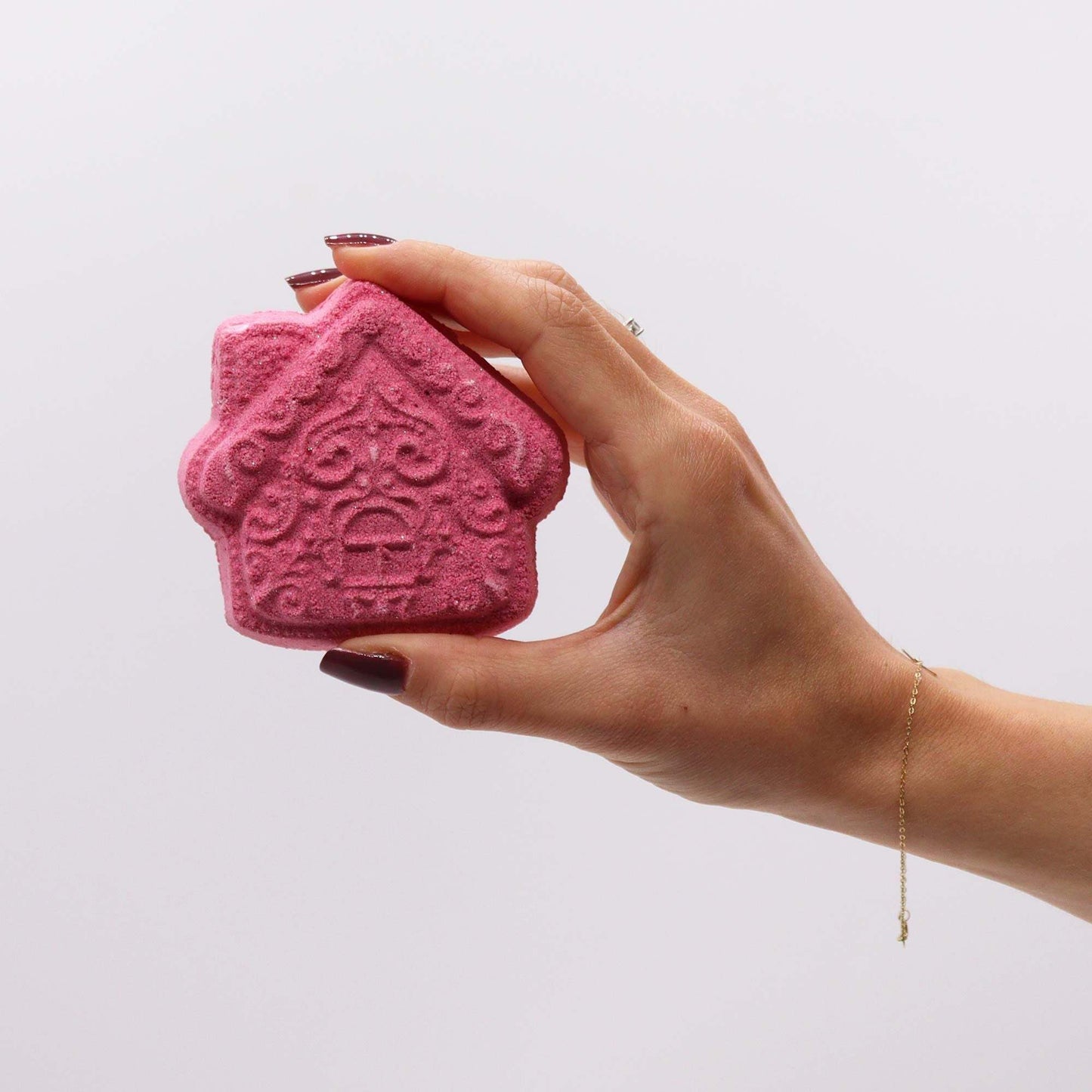 Hand holding pink gingerbread house shaped Christmas bath bomb from festive gift pack