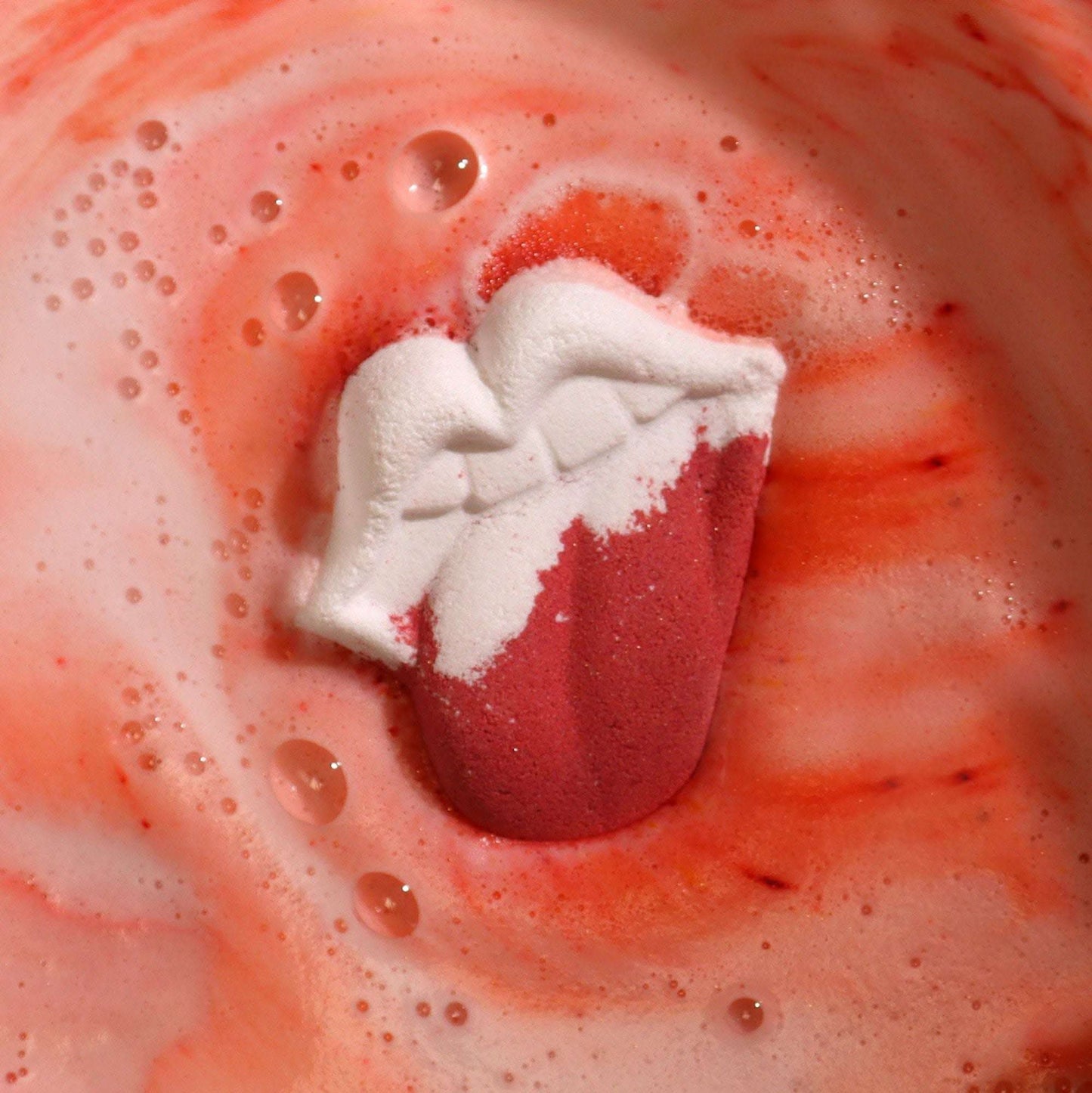 Lips shaped bathbomb dissolving in water with raspberry and pomegranate foam
