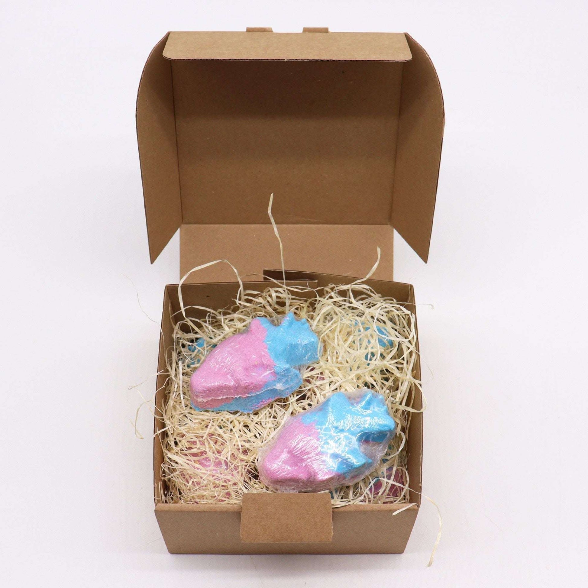Dinosaur bathbombs in pink and blue with blueberry scent in a brown gift box with straw filling