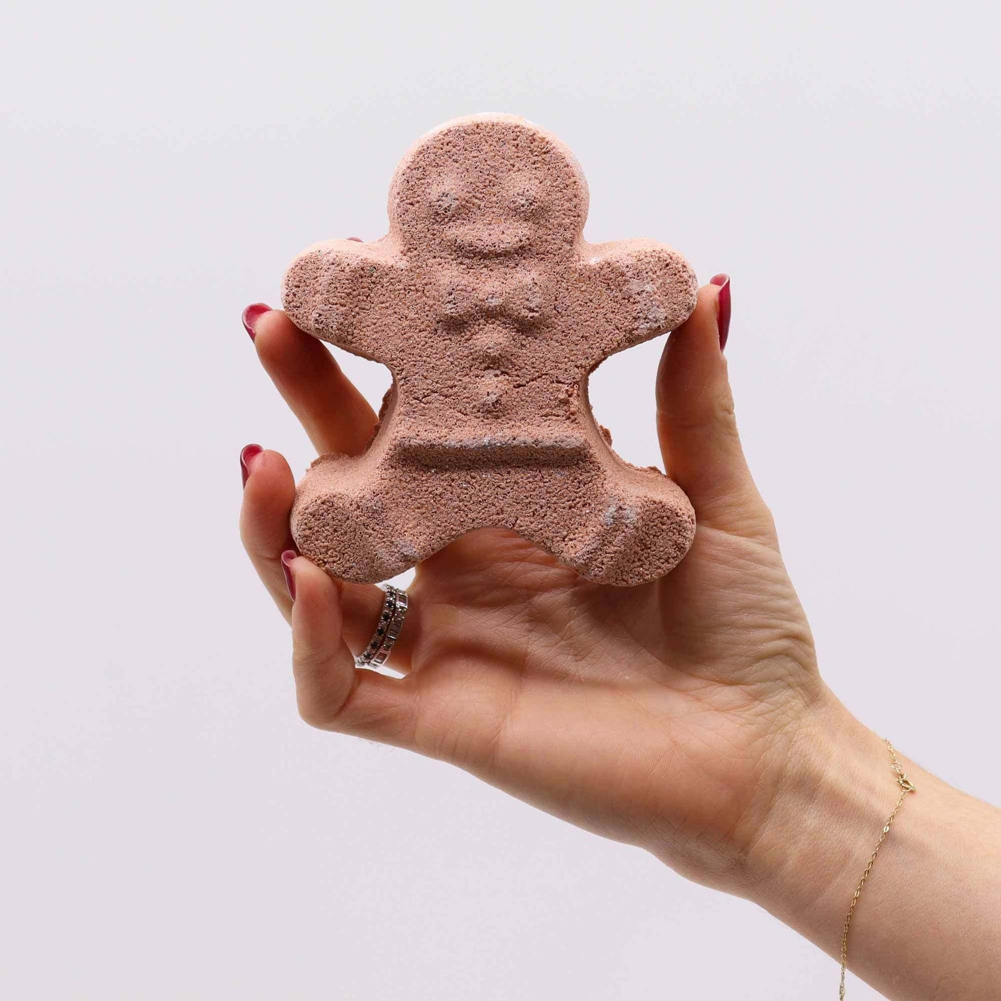 Hand holding gingerbread-shaped Christmas Fun Bath Bomb with warm gingerbread scent