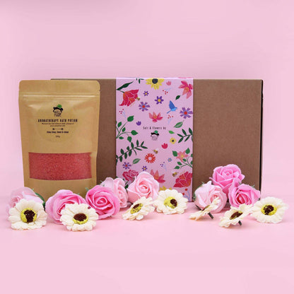 Salt Soak Set with natural pink bath salts and floral packaging surrounded by pink and white flowers on pink background