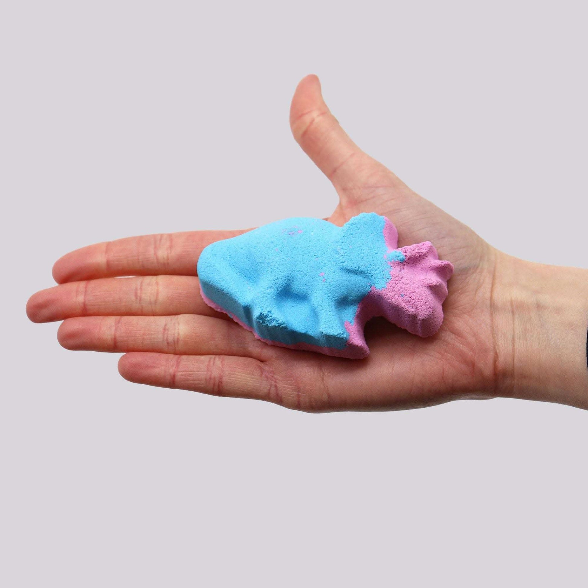 Blue and pink dinosaur shaped blueberry scented bath bomb held in hand