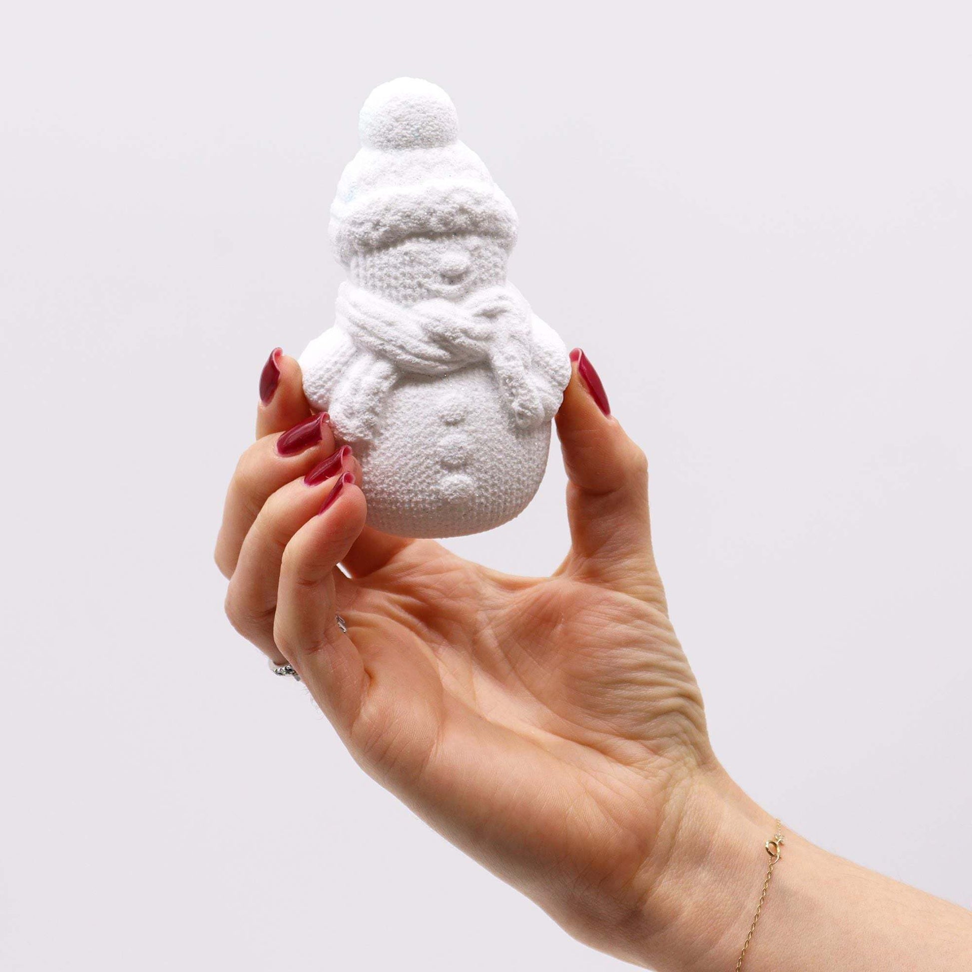 Hand holding white snowman shaped Christmas Fun Bath Bomb with knitted hat and scarf design