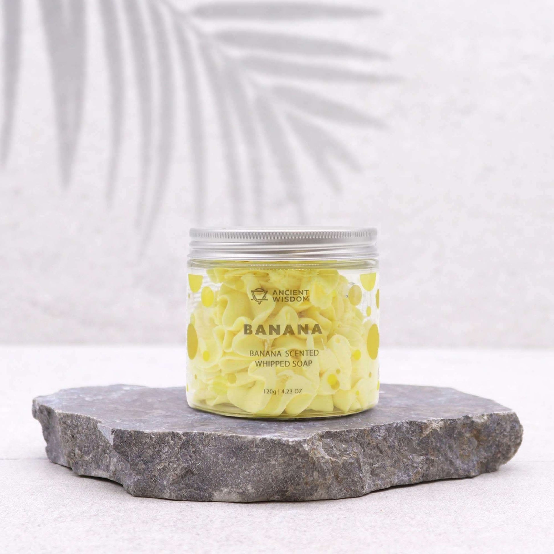 Banana scented fruity whipped soap in clear jar on stone slab for gentle skincare and spa-like pampering