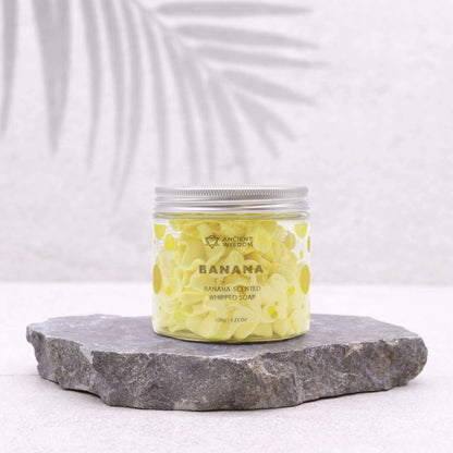 Banana scented fruity whipped soap in clear jar on stone slab for gentle skincare and spa-like pampering