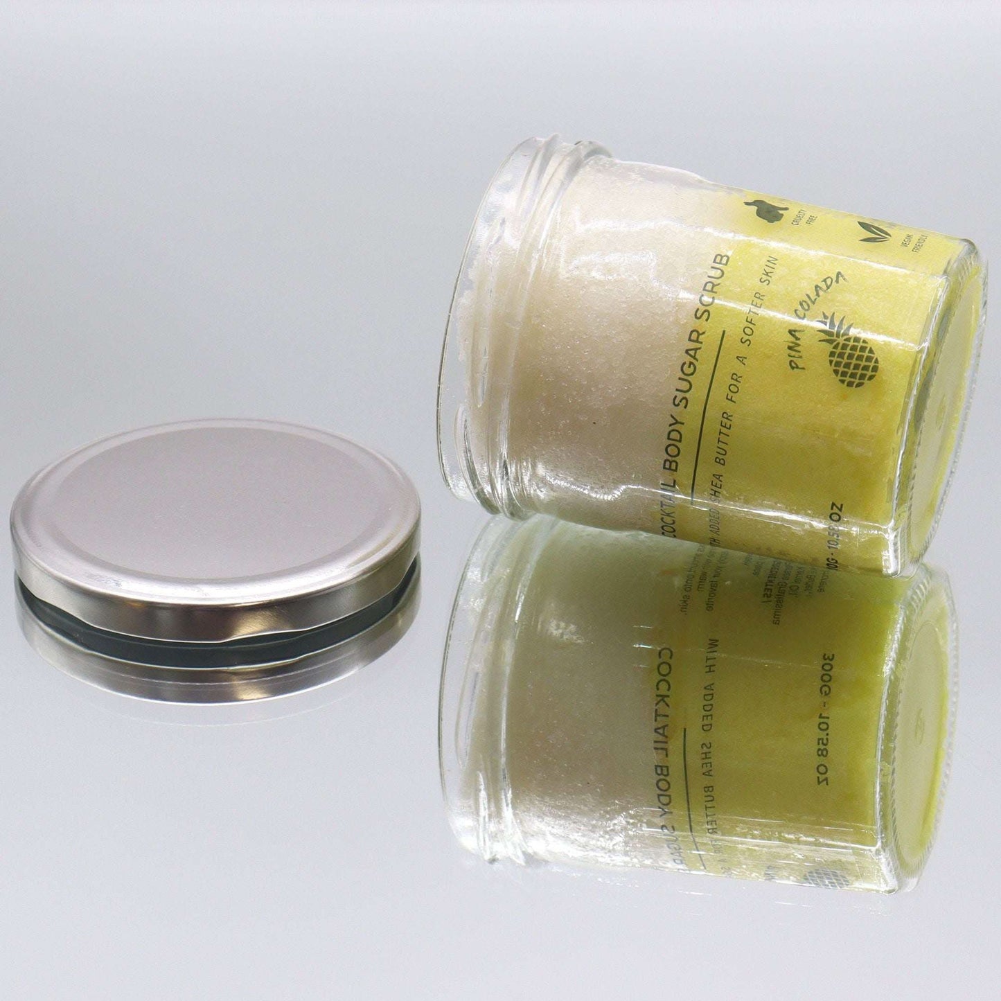 Fragranced sugar body scrub in clear jar with silver lid, pinacolada scent, 300g container