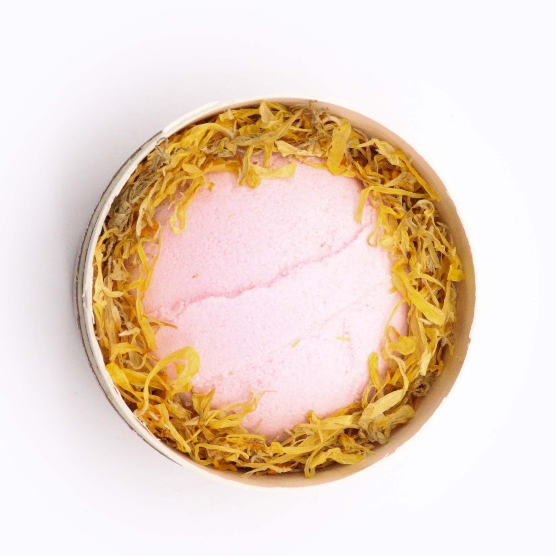 Blooming Pink Bliss pink bath bomb surrounded by marigold petals in circular packaging for aromatherapy and self-care ritual