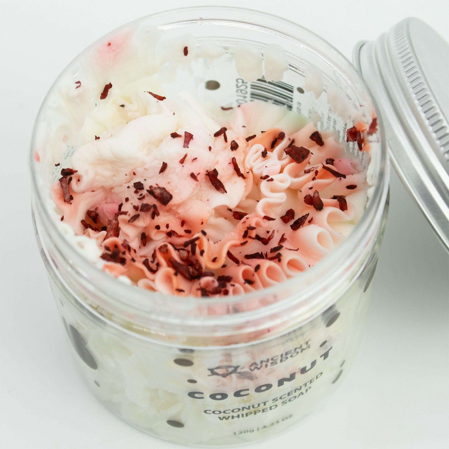 Open jar of coconut whipped soap with white and pink mousse texture topped with coconut shavings