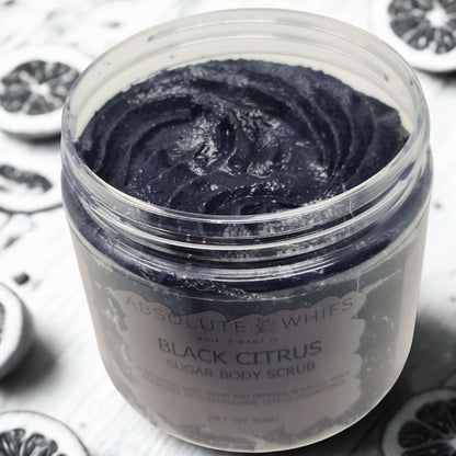 Black Citrus Sugar Body Scrub with dark textured exfoliant in a jar surrounded by black citrus slices