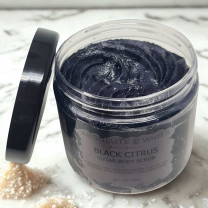 Black Citrus Sugar Body Scrub in a clear jar with a black lid showing dark purple textured scrub inside and spilled sugar granules nearby