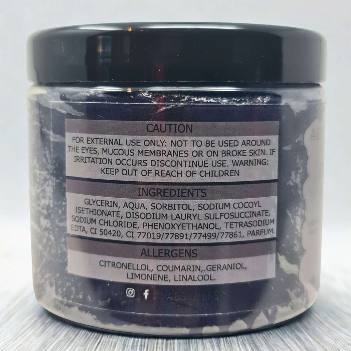 Black Citrus Sugar Body Scrub jar showing caution label, ingredients list, and allergen information on a dark container with black lid