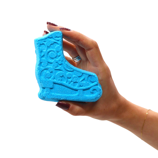 Blue ice skate shaped bath bomb with embossed detailing, held in a hand showcasing the Break the Ice Christmas Bath Bomb Gift Pack