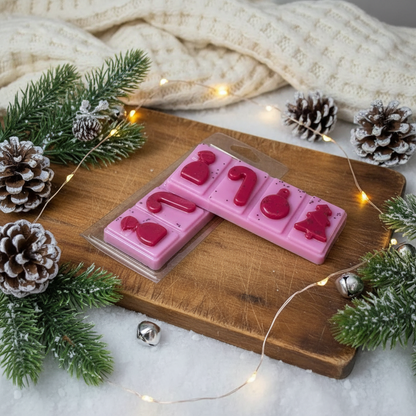 Candy Cane Wax Melt Snap Bar in pink with red holiday shapes including candy cane, snowflake, and tree in festive packaging on wooden board