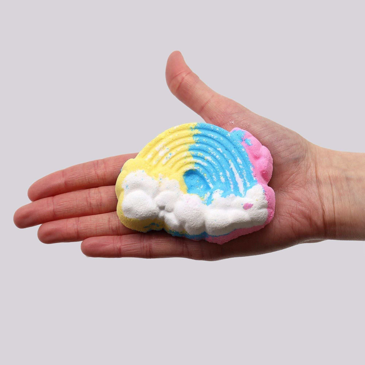 Cloud Bath bomb held in a hand, shaped like a cloud with colorful pastel segments in yellow, blue, pink, and white foaming texture