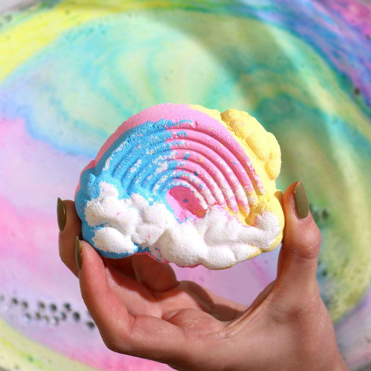 Cloud Bath bomb in rainbow colors with white foamy clouds and a textured pattern held in hand against a colorful bath water background