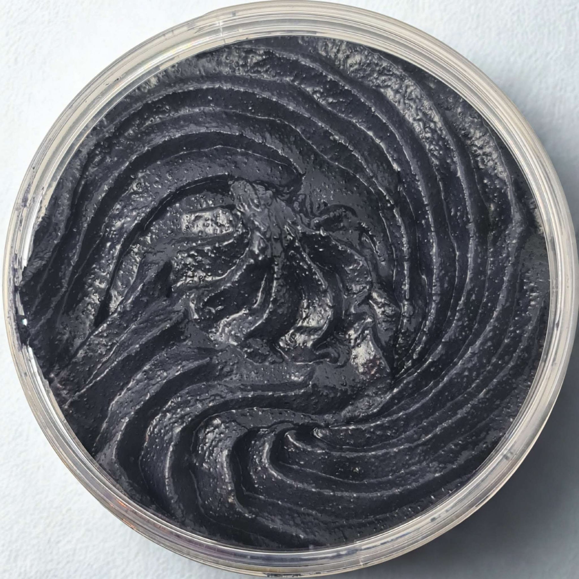 Top view of black citrus sugar body scrub in a clear container showing textured swirl pattern