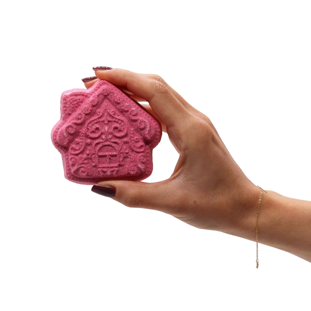 Gingerbread Town Christmas Bath Bomb Gift Pack featuring a hand holding a pink house-shaped bath bomb with intricate patterns
