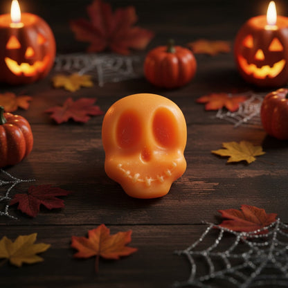 Absolute Whifs orange skull-shaped wax melt on a dark wooden table with autumn leaves, spider webs, and jack-o-lanterns