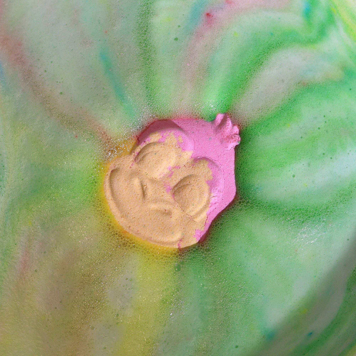 Monkey Bath bomb with playful monkey face shape in pink and yellow colors dissolving in green and pink swirling bath water