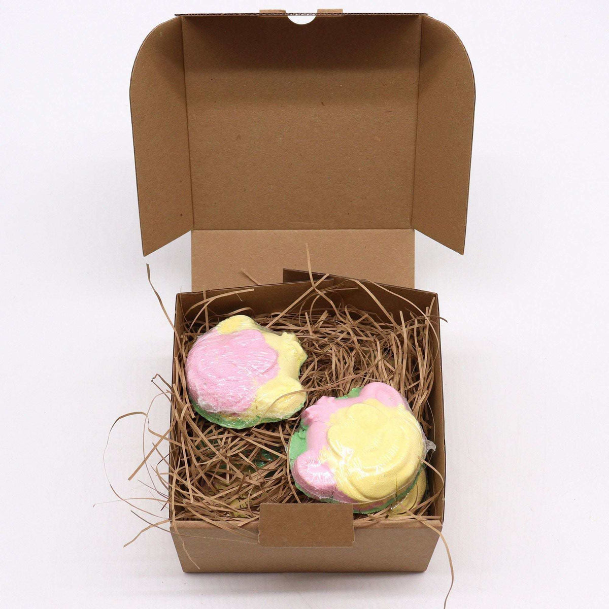 Monkey Bath bomb set with two pastel pink, yellow, and green monkey-shaped bath bombs in a brown cardboard gift box with straw filler