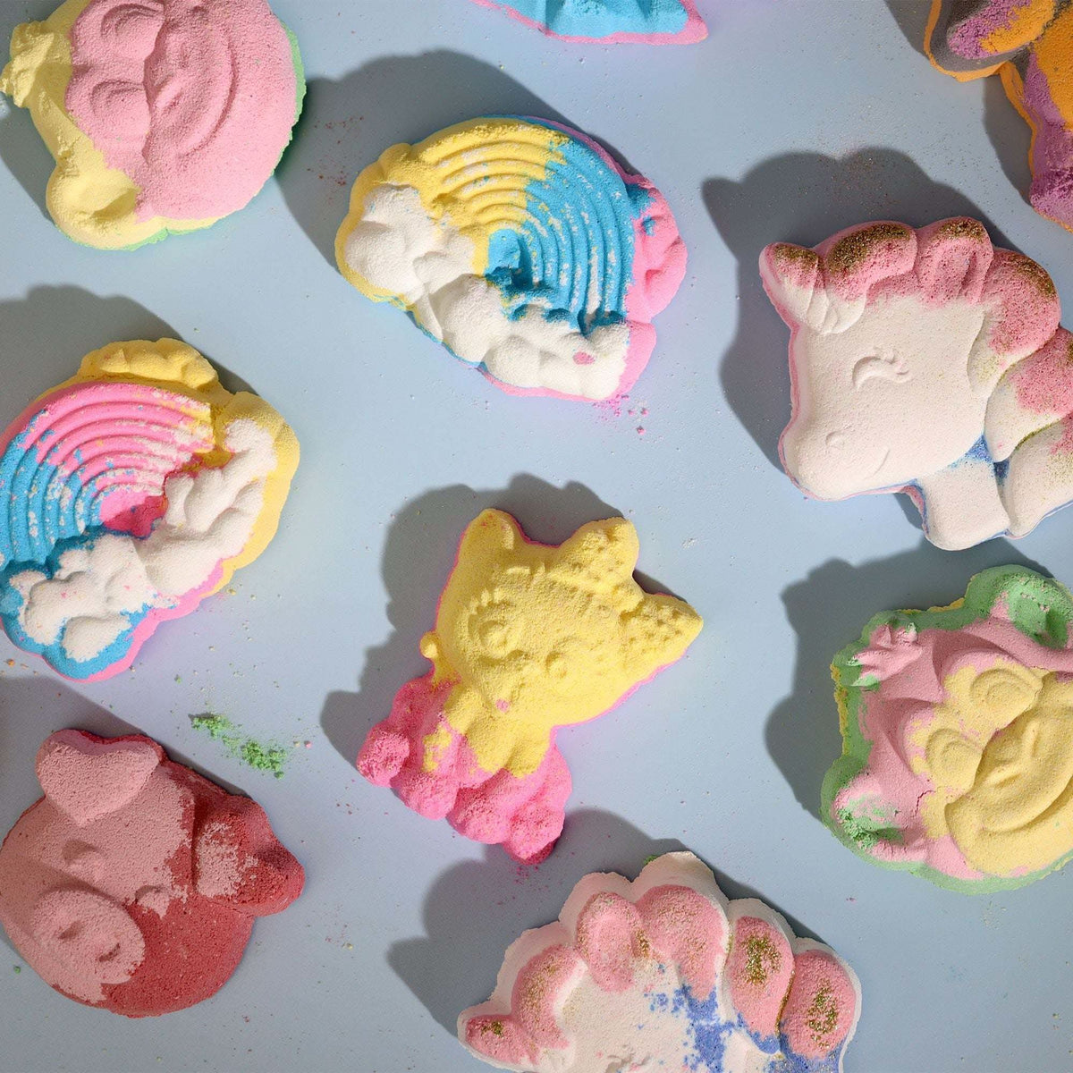 Monkey Bath bomb shaped like a yellow giraffe among colorful rainbow, unicorn, and other whimsical pastel bath bombs on a light blue surface