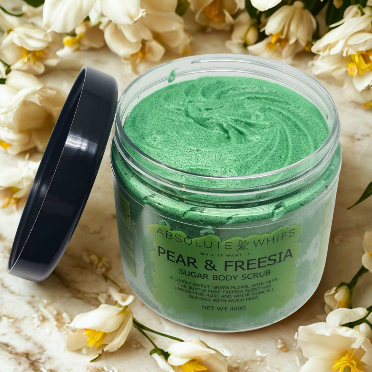 Pear and Freesia Sugar Body Scrub in a clear jar with green whipped texture and black lid, surrounded by white freesia flowers