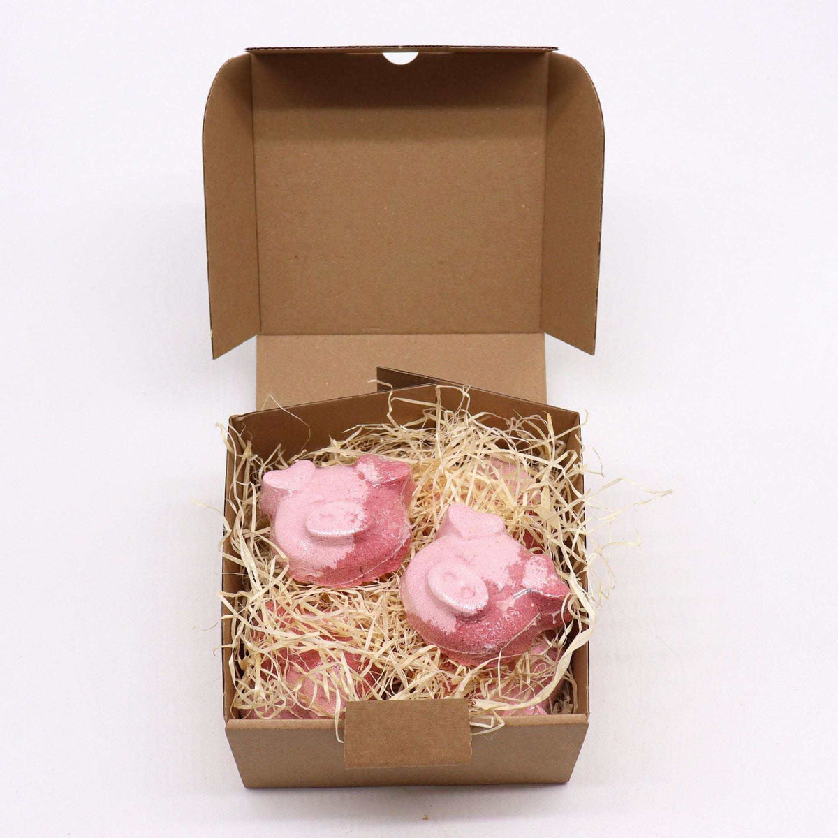 Pig Bath bomb shaped like cute pink pigs with detailed features, nestled in natural straw inside a brown cardboard box