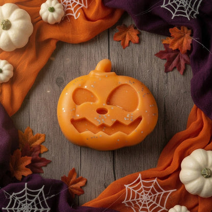 Absolute Whifs pumpkin-shaped wax melt with glitter on a wooden table surrounded by orange fabric and mini pumpkins.