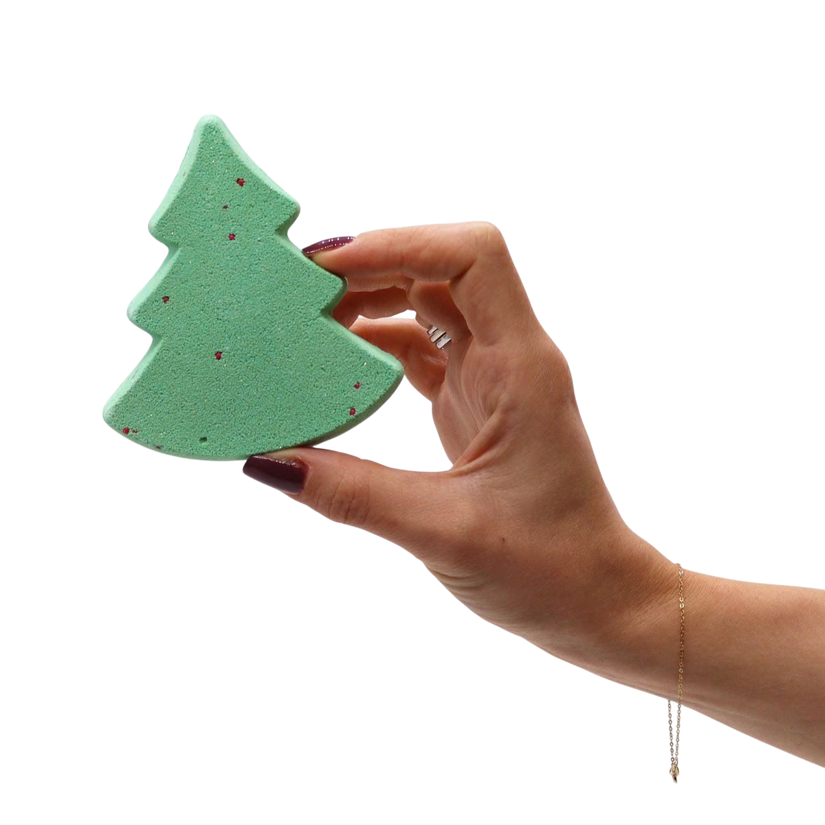 Green Christmas tree shaped bath bomb with red speckles held by a hand, part of the Silent Night Christmas Bath Bomb Gift Pack