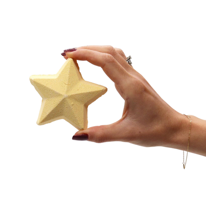 Star-shaped pale yellow bath bomb held in hand with polished nails, part of the Silent Night Christmas Bath Bomb Gift Pack