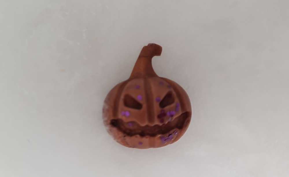 Halloween pumpkin-shaped wax melt with brown color and purple glitter.